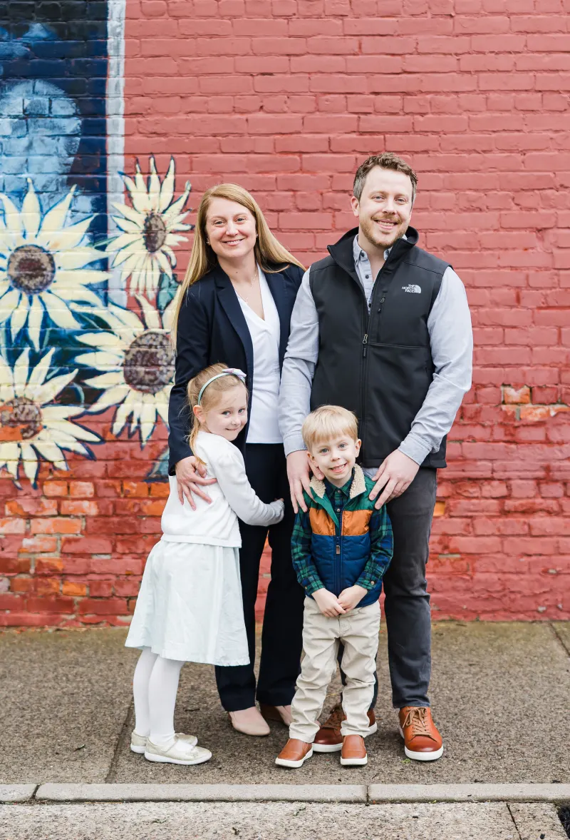 Alissa Brennan with her husband and two children in front of a sunflower mural in Rochester